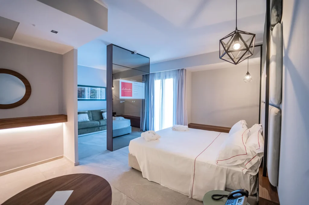 Nell'immagine si vede un salottino con un divano e dietro la parete la camera con letto matrimoniale.