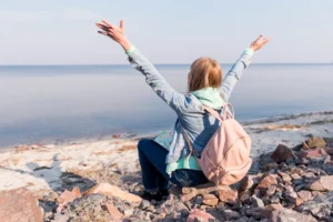 Nell'immagine una ragazza seduta sugli scogli di fronte al mare.